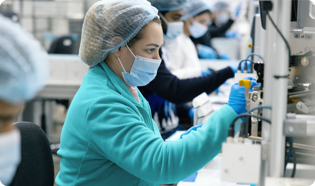 Healthcare workers in protective clothing and masks operate machinery in a LetsGetChecked manufacturing and distribution facility. 