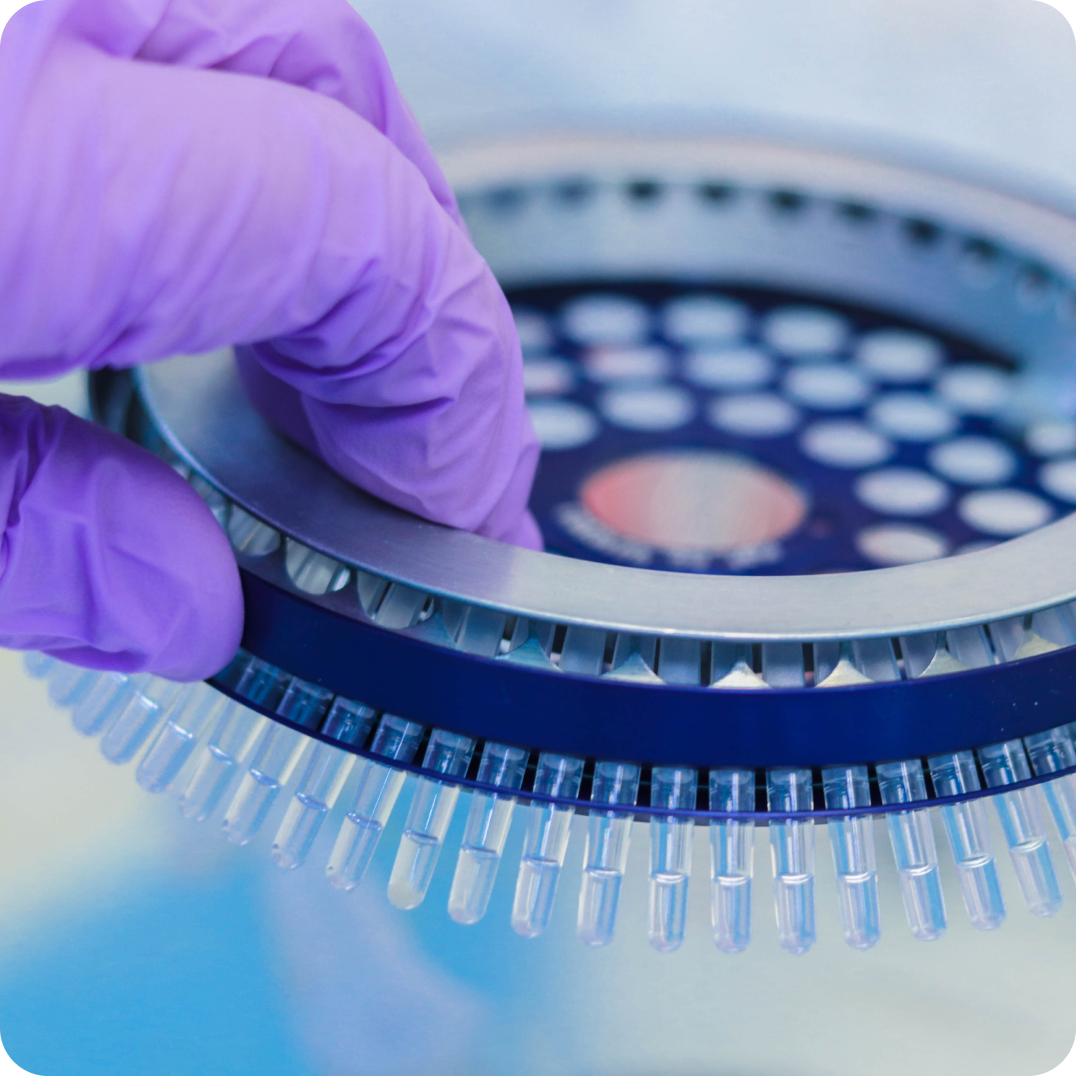 Gloved hand placing a sample into a laboratory centrifuge for processing.