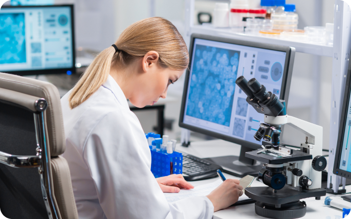 Scientist analyzing data through a microscope and computer screen in a lab.