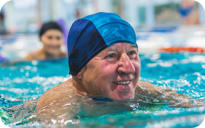 Smiling older man wearing a swimming cap while he swims in a pool.