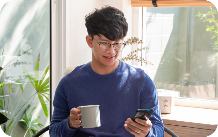 Young man holding a smartphone in one hand and a mug in the other.