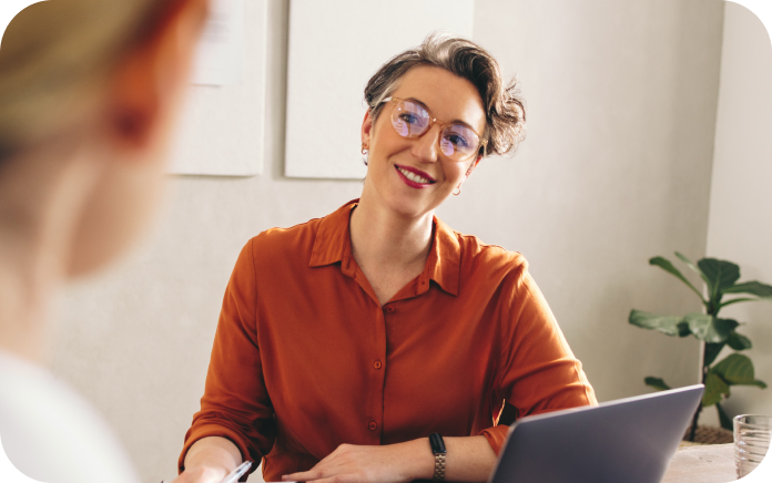 Smiling woman sitting at her desk with an open laptop.