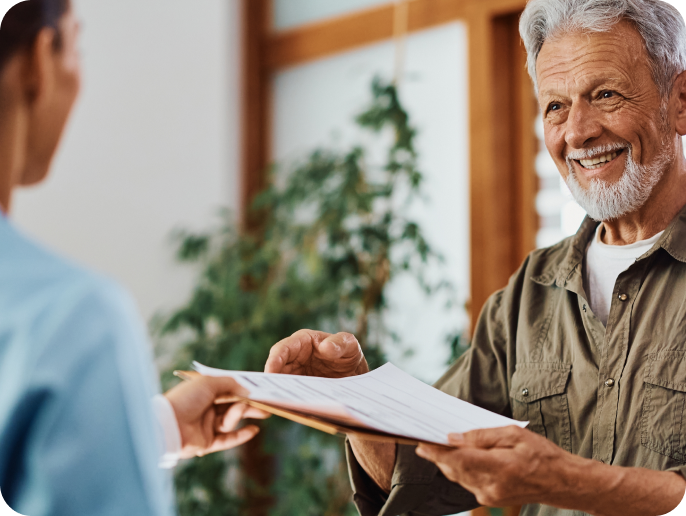 Smiling older man receiving a document from a medical staff member.