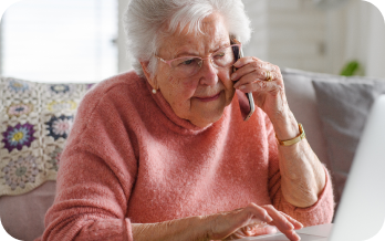 Elderly woman talking on the phone while sitting on her sofa.