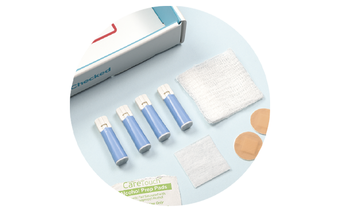 Kit contents being taken out of box. Lancets, gauze, alcohol wipes, and finger band aids laid out.