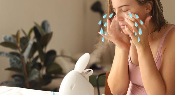 A woman gets mist on her face as she sits in front of a facial steaming machine