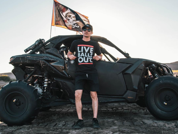 Man wearing a shirt that says 'Live Balls Out' stands in front of an off-road vehicle