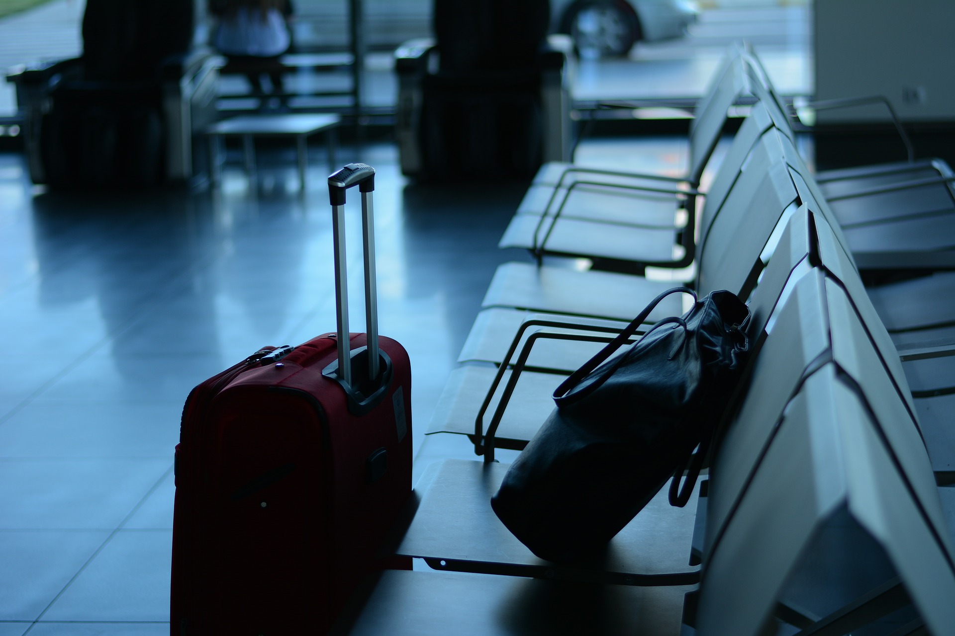 a red suitcase sits on a white floor next to a row of white chairs