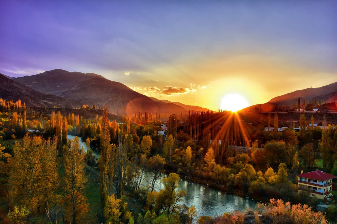 a river running through a valley with trees and a sunset