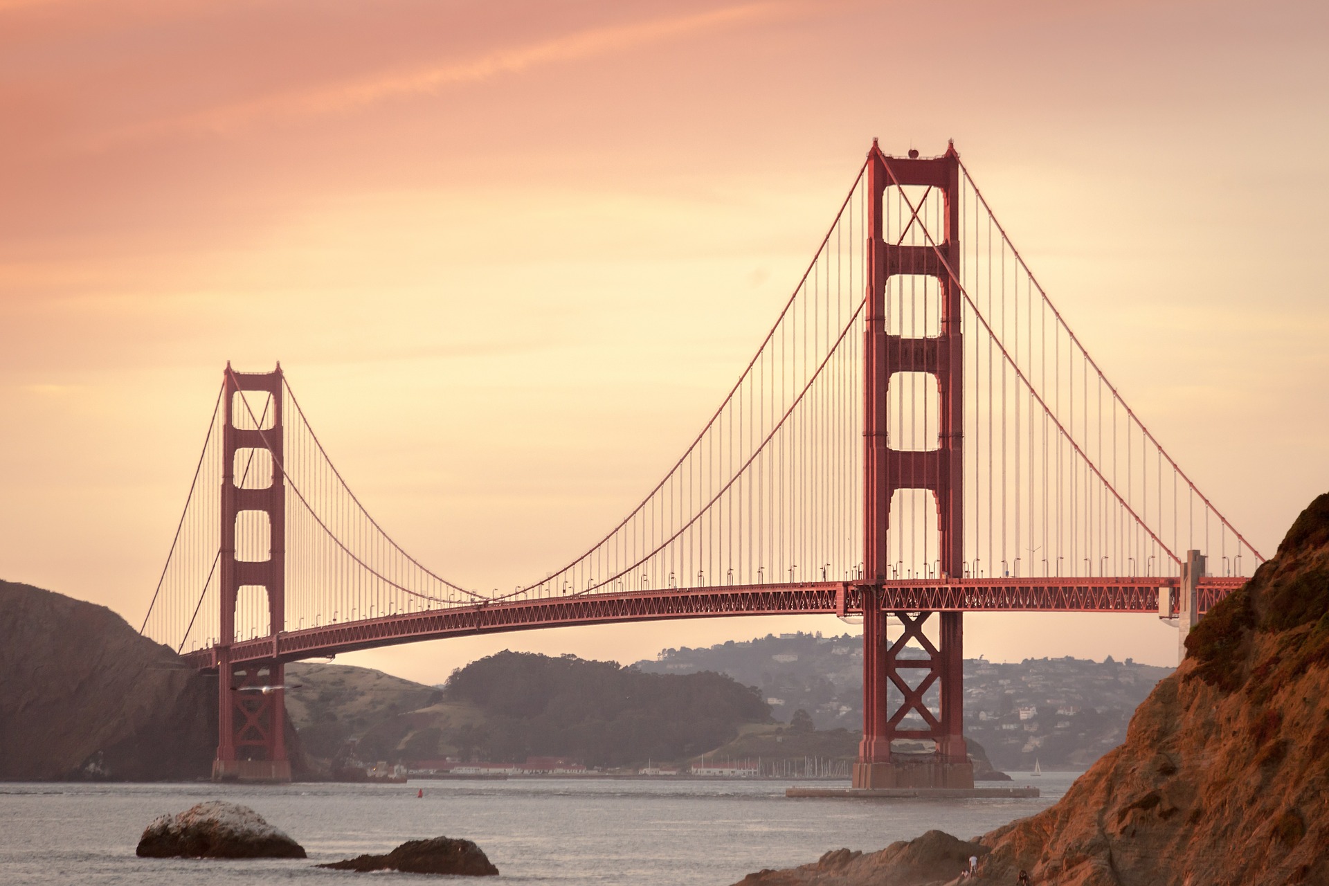 a red bridge with a body of water in the background with Golden Gate Bridge in the background