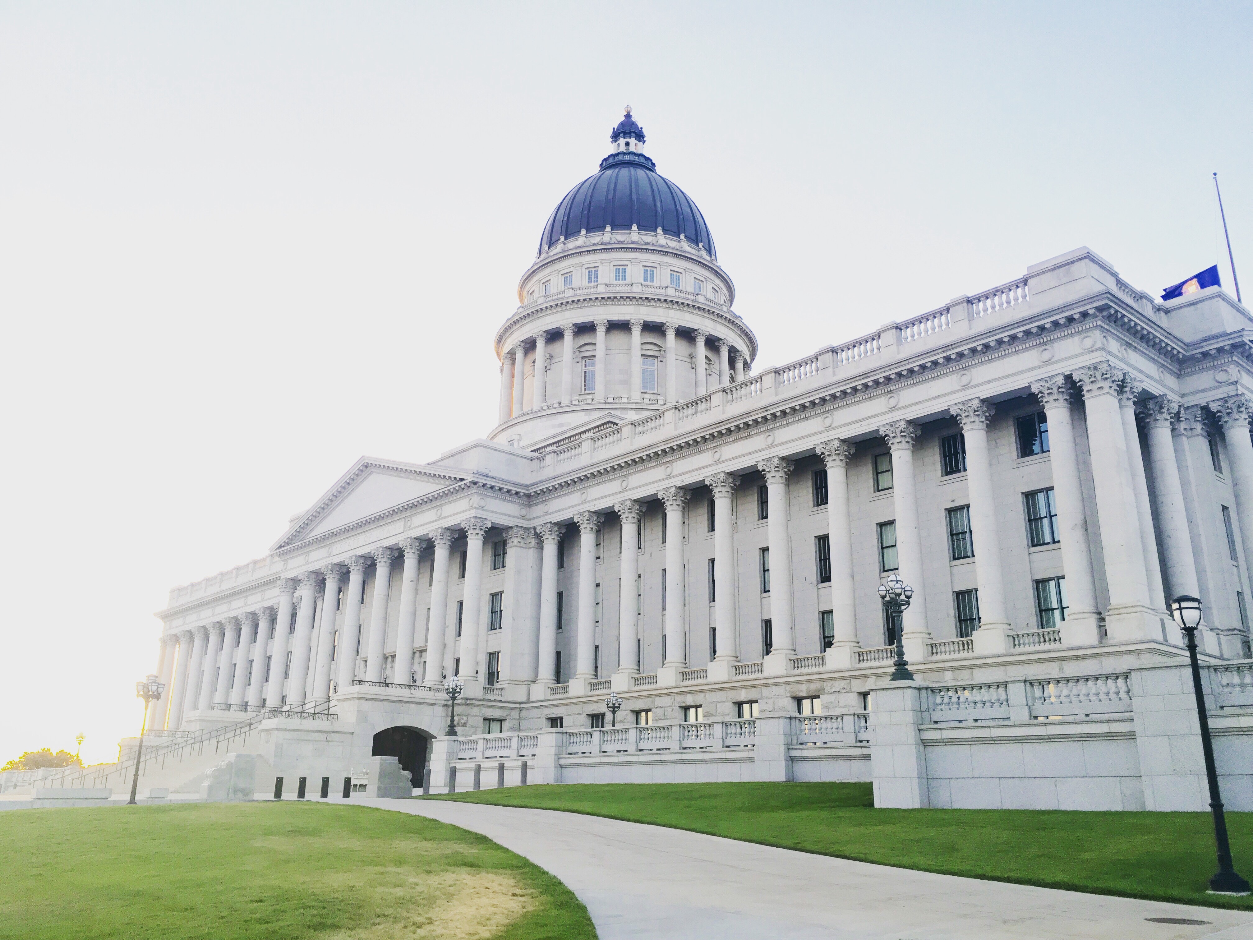 a large white building with columns with Utah State Capitol in the background