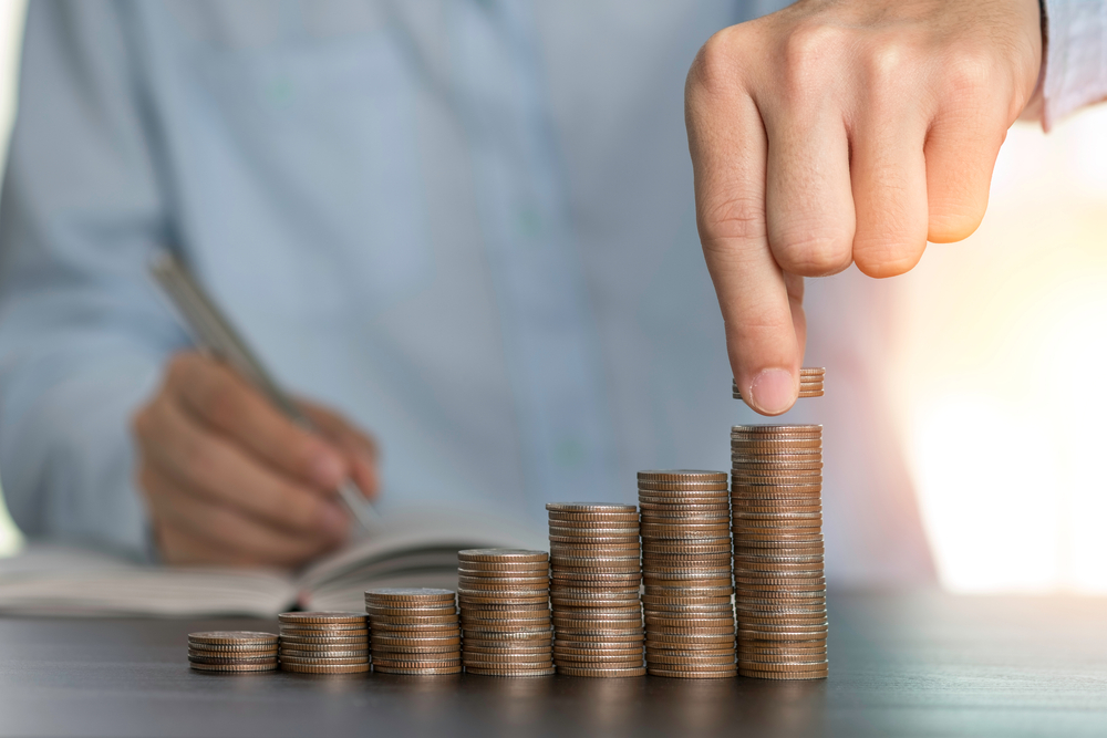 a person holding a pen over a pile of coins