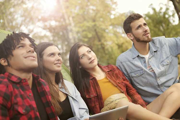 Cheerful young men and women with tablet looking away in a park
