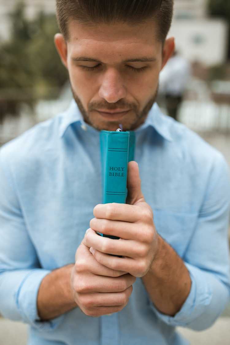 Man in blue button shirt, eyes closed, holding a Holy Bible