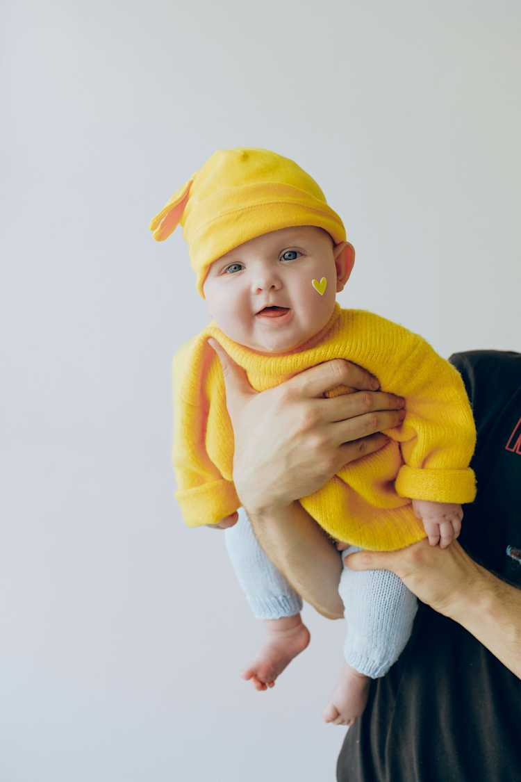 Crop parent holding smiling baby in arms against gray wall in a room