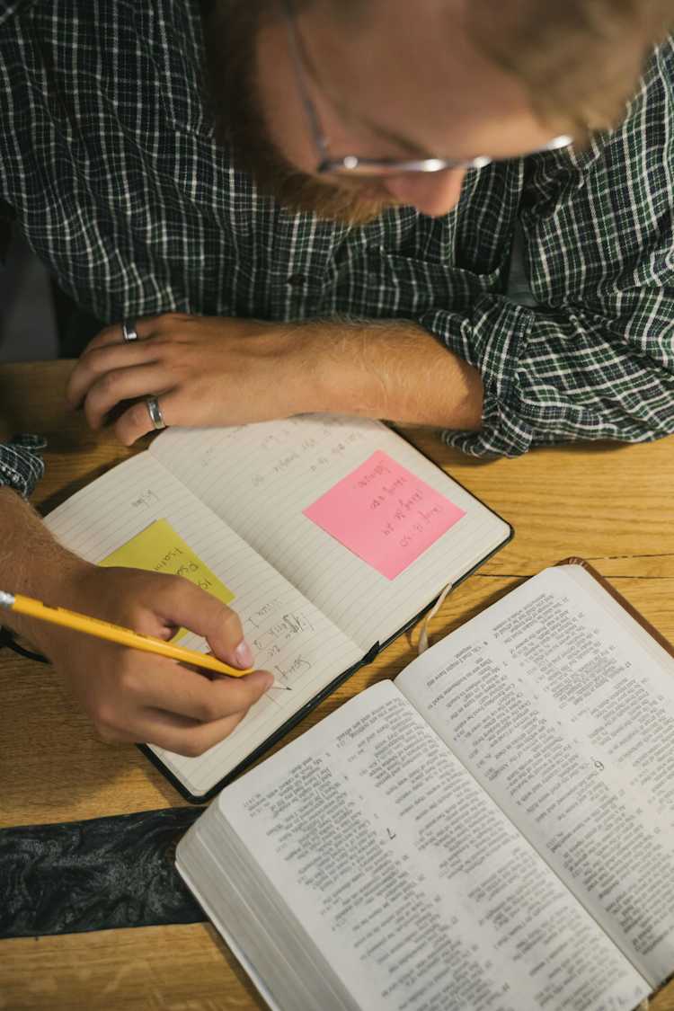 A man writing on a notebook while reading a Bible