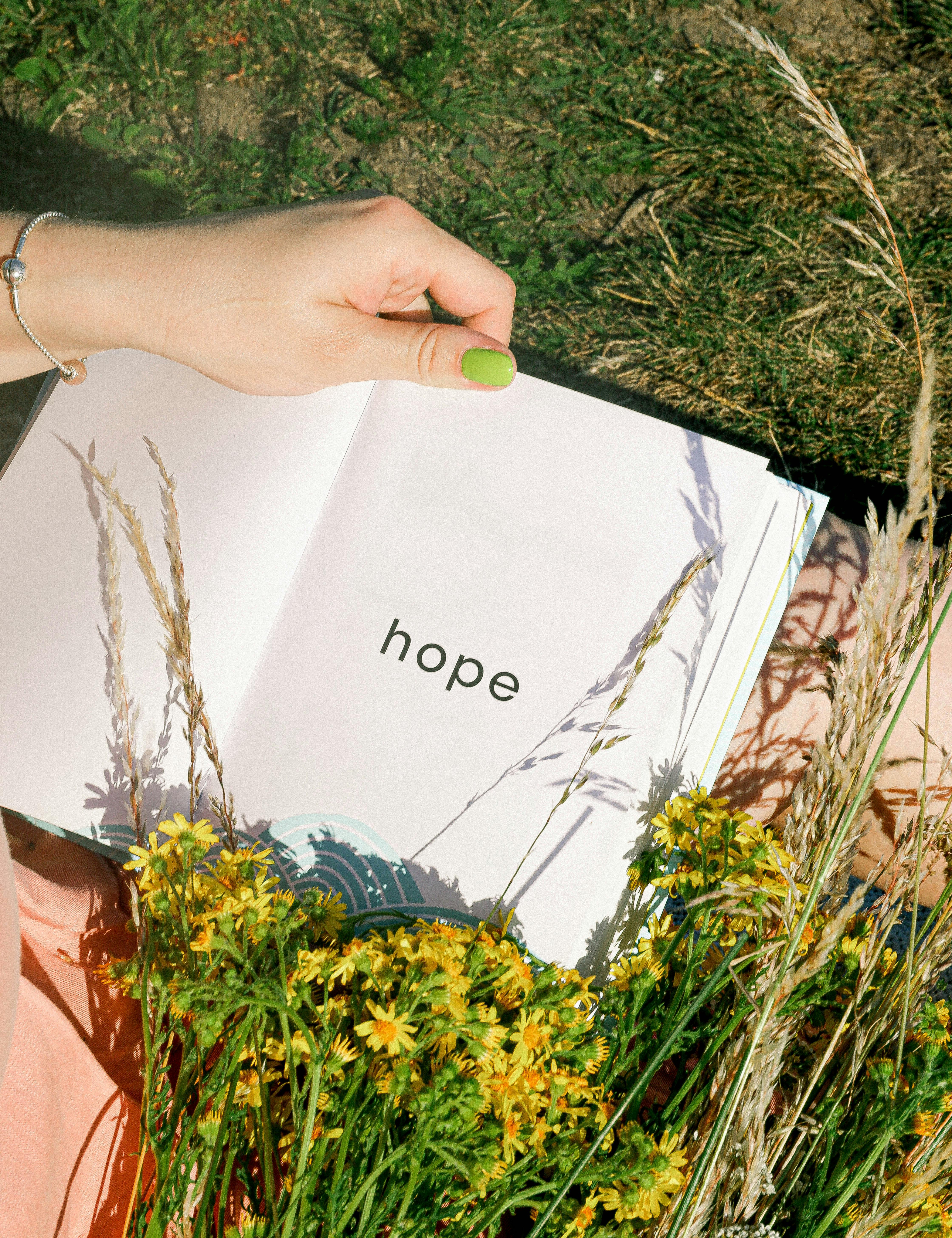Woman holding a book with the word hope it in a grass field with yellow flowers