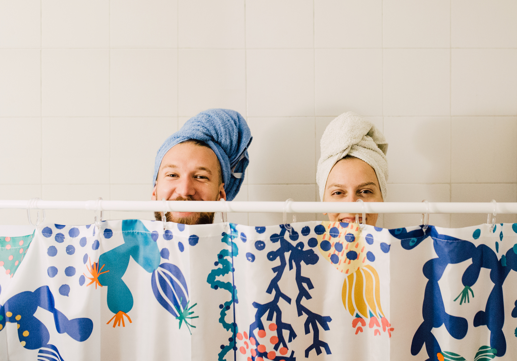 Image of a couple sticking their heads out from the top of the shower curtain with towels on their heads.