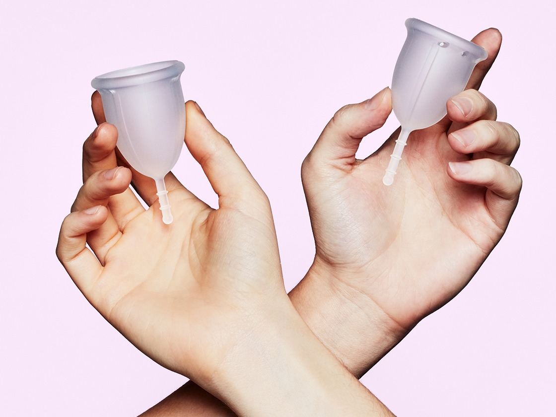 two hands each holding one clear menstrual cup in different sizes
