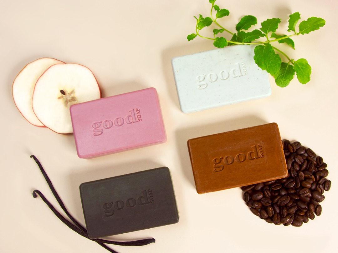 Image of 4 Alaffia bar soaps including African bar soap with apple, coffee beans, and mint in the background