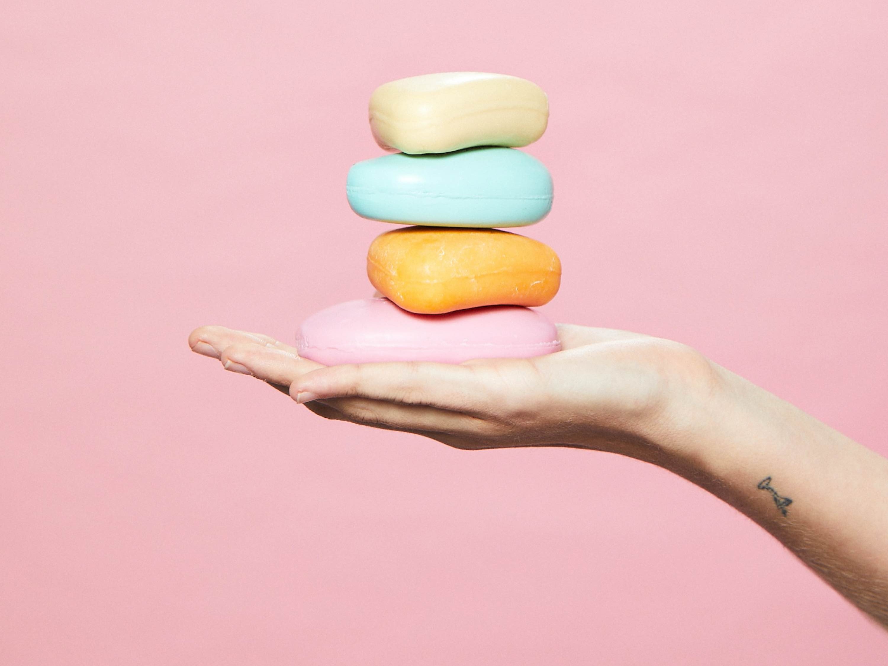 Photo of hand holding bar soaps against pink background