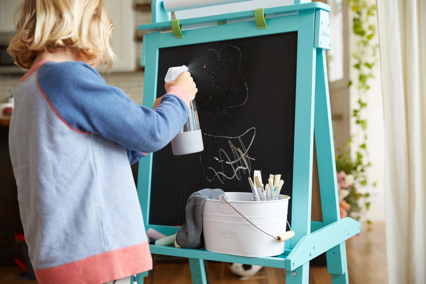 blonde child spraying chalkboard with cleaner from a glass bottle