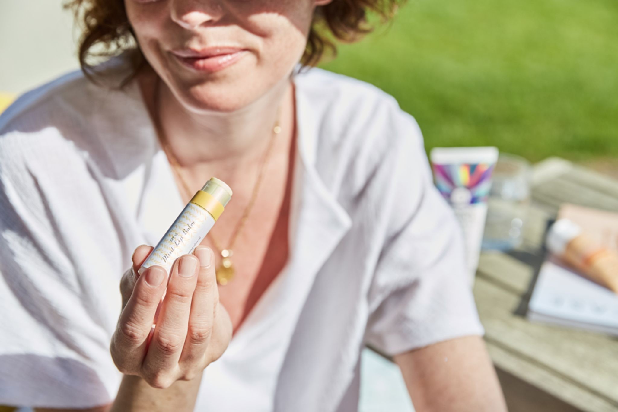 A person in a white shirt holding a tube of lip balm.