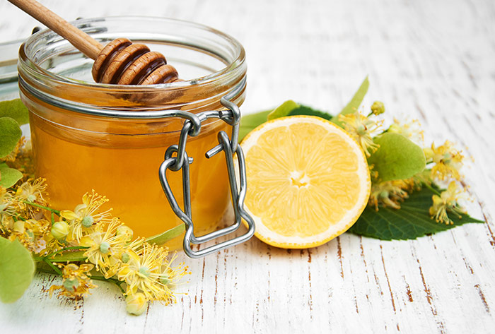Image of a jar of honey next to a lemon.
