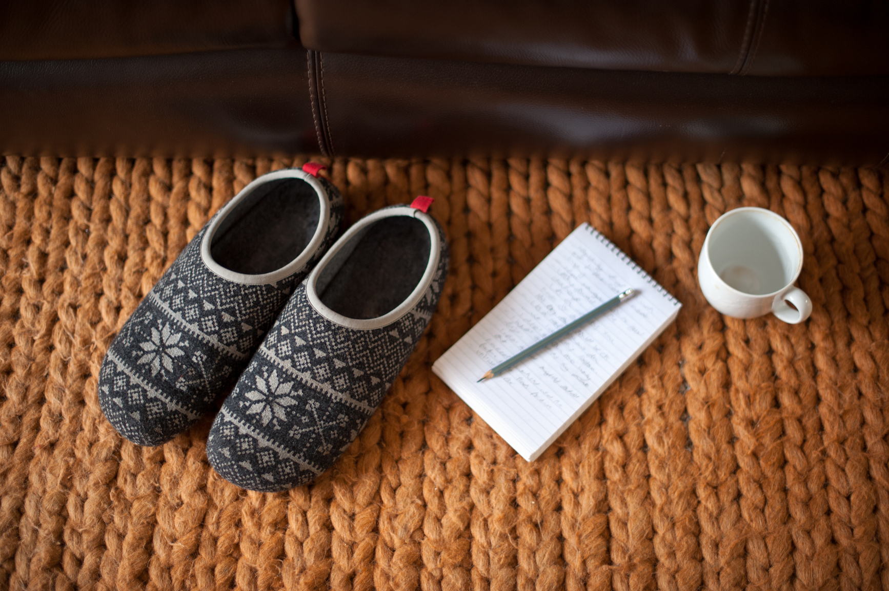 Image of slippers next to pencil and paper and mug on orange blanket