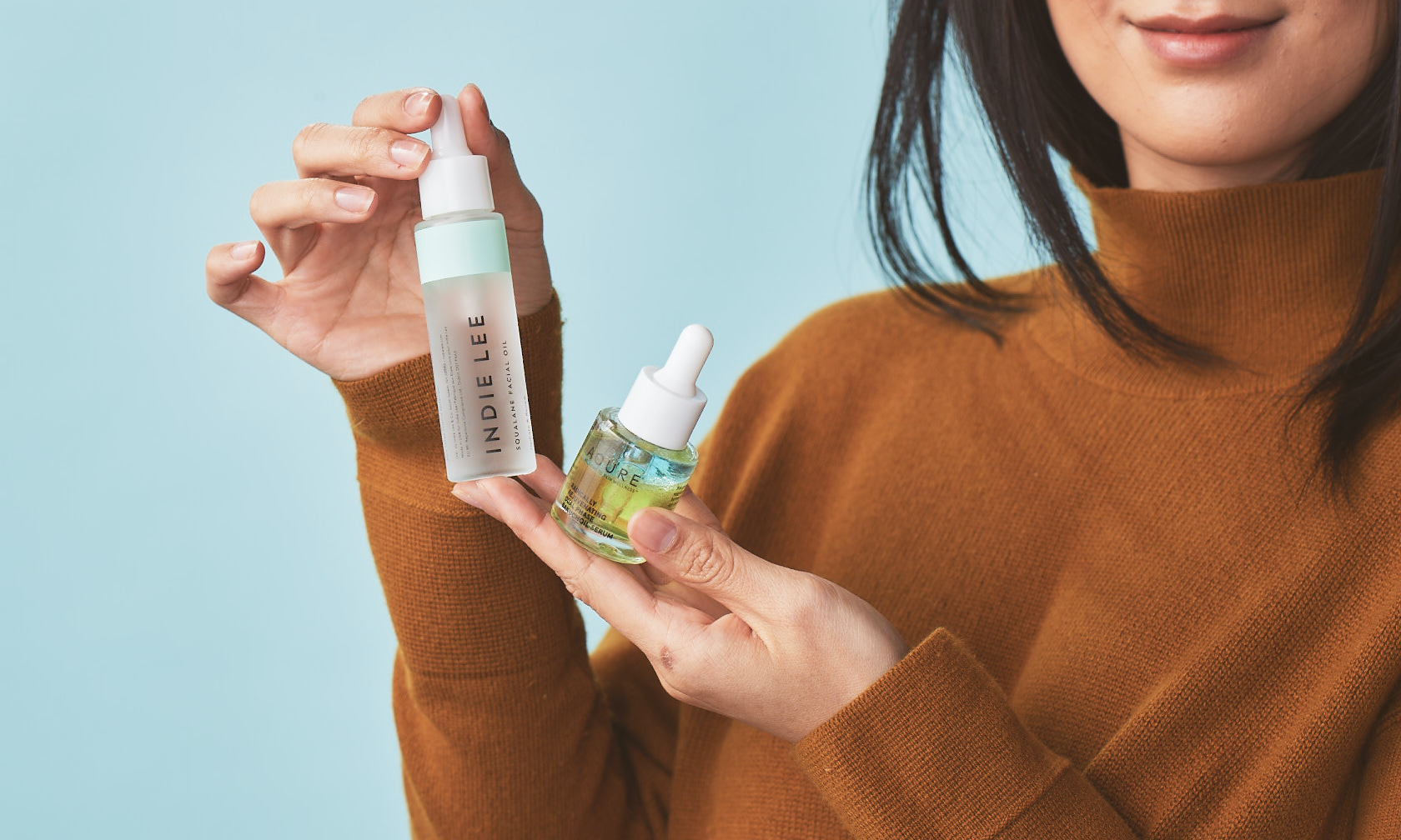 Photo of two skincare serums being held up by woman in orange turtleneck