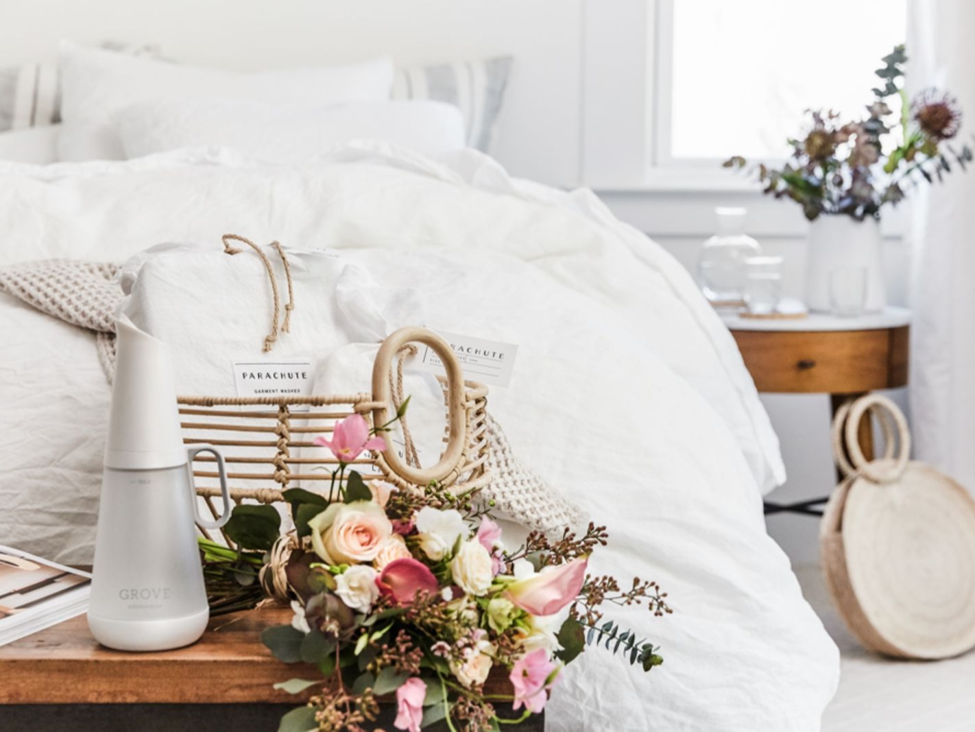 Image of bed with fluffy white comforter and flowers and Grove products on bench at end of bed