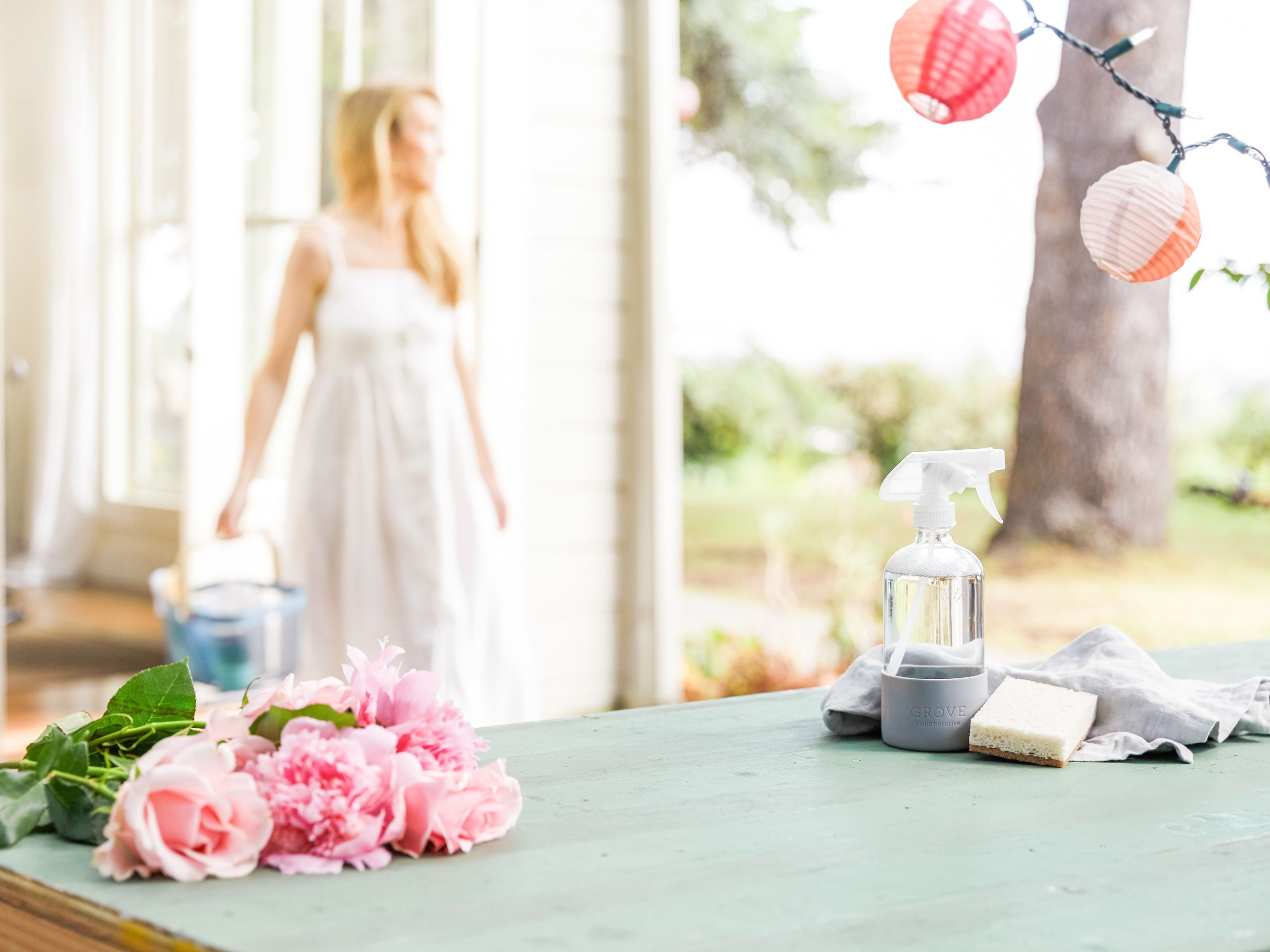 Woman in white dress in background next to open door with table and roses and string lights in foreground