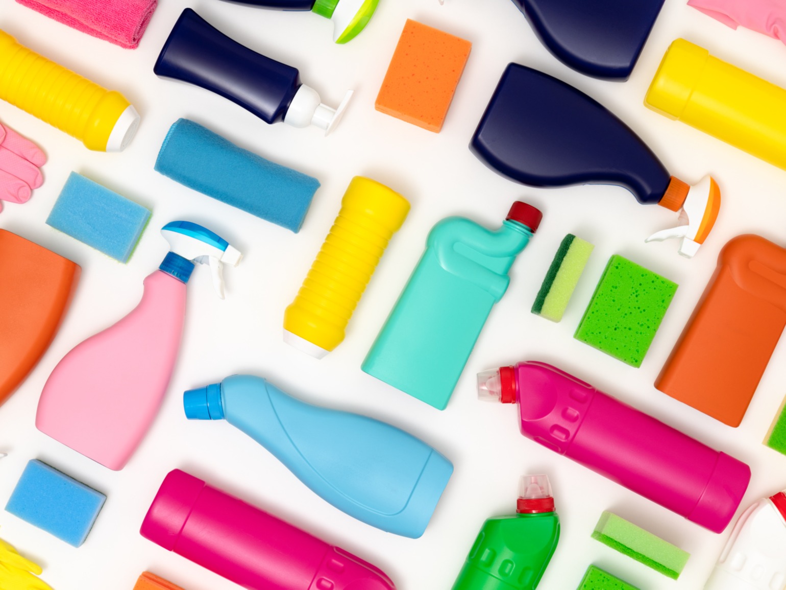 Several colorful spray and pour bottles lying in diagonals next to each other on white background with sponges in between