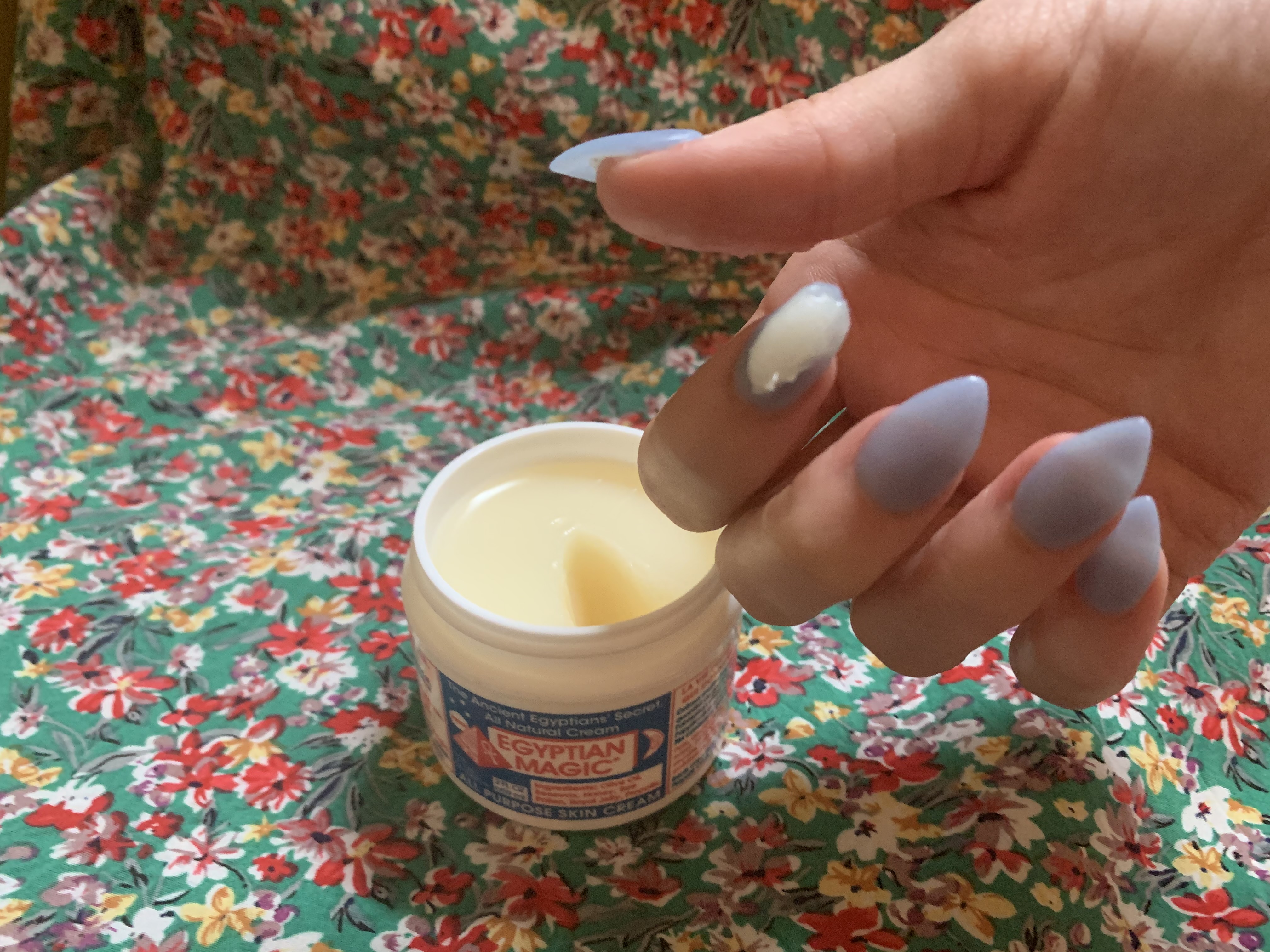 Photo of open jar of Egyptian Magic cream and hand with cream on finger