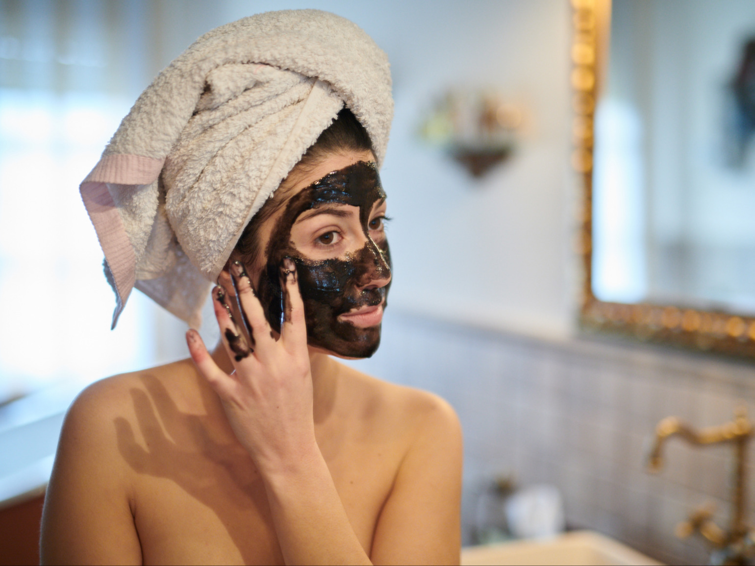 Photo of woman wearing charcoal face mask and towel on head