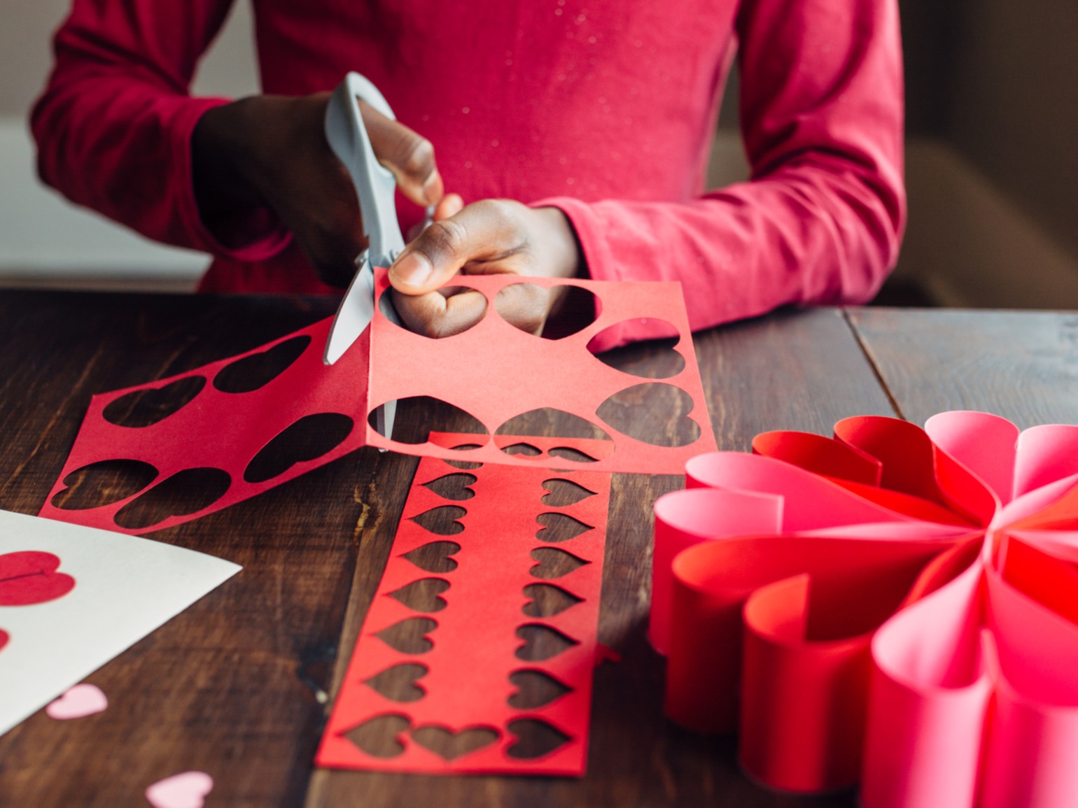 Kid cutting out red paper hearts at table