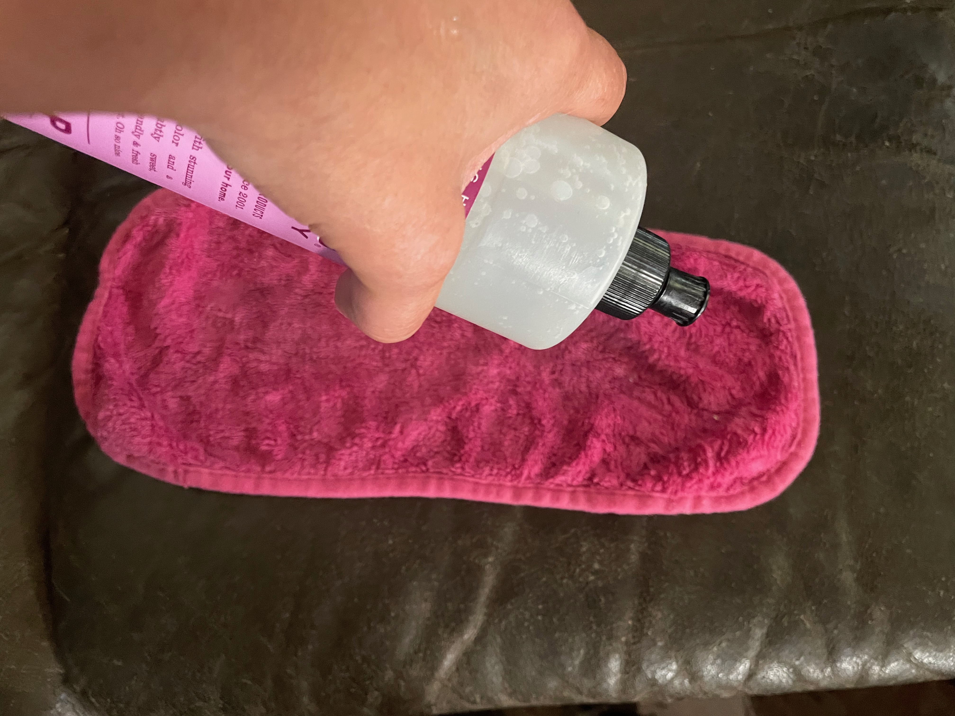 A hand adding soap to a microfiber cloth to scrub a leather couch.