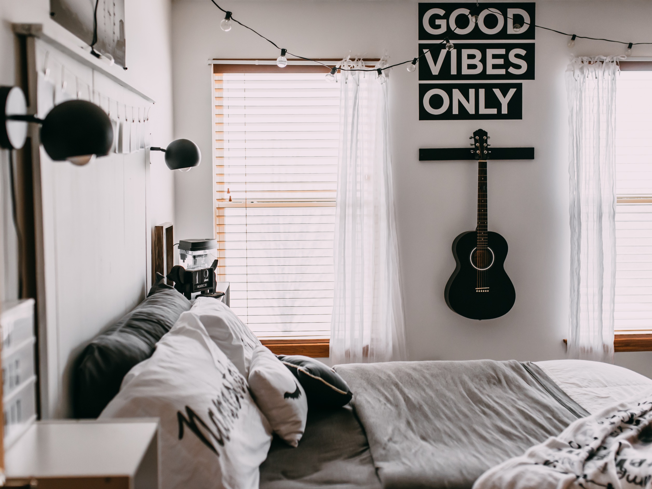 clean dorm room with guitar on the wall, string lights, and wall art that says "good vibes only"