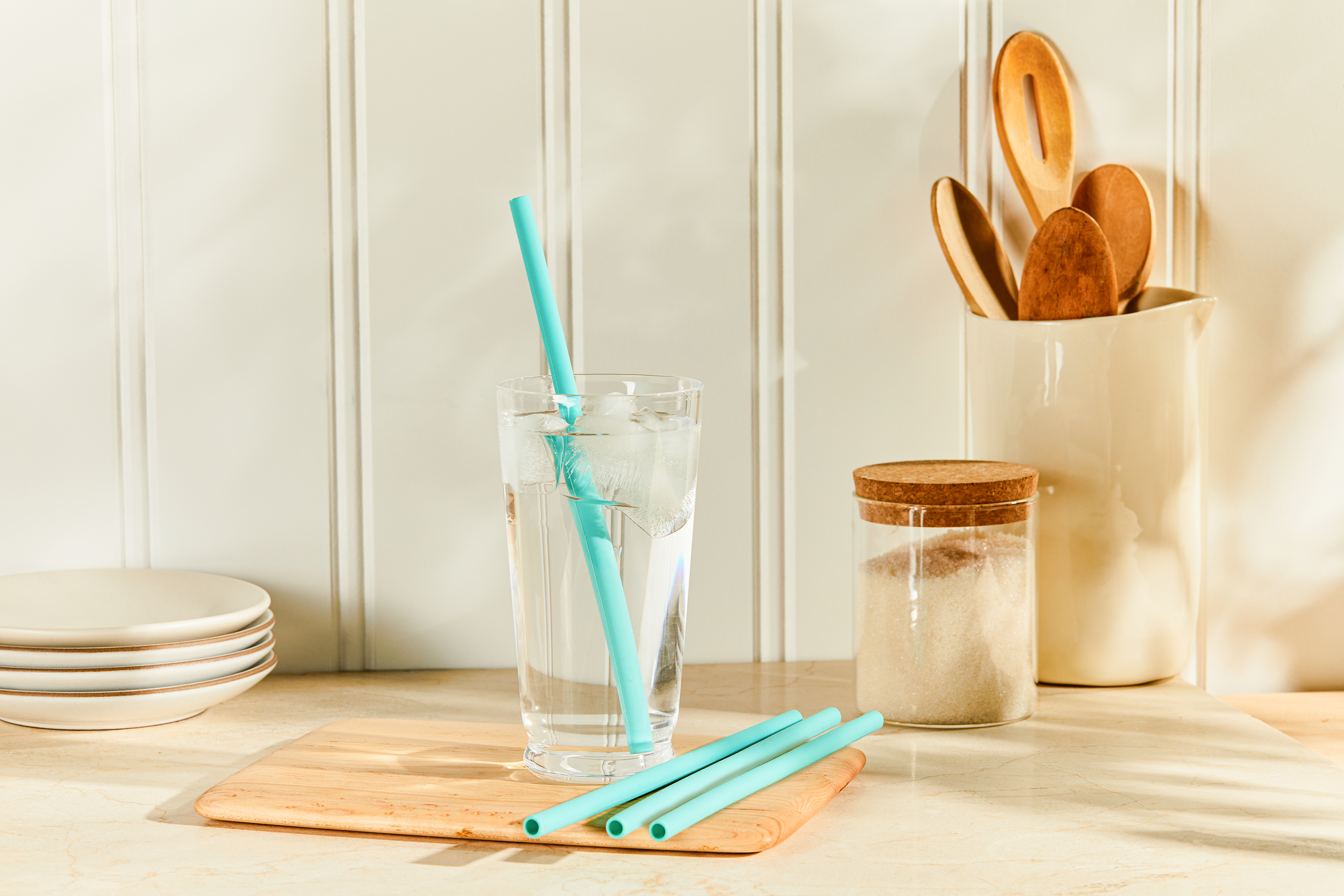 Image of 4 aqua silicone straws. 3 on the counter and one in a glass of ice water. 