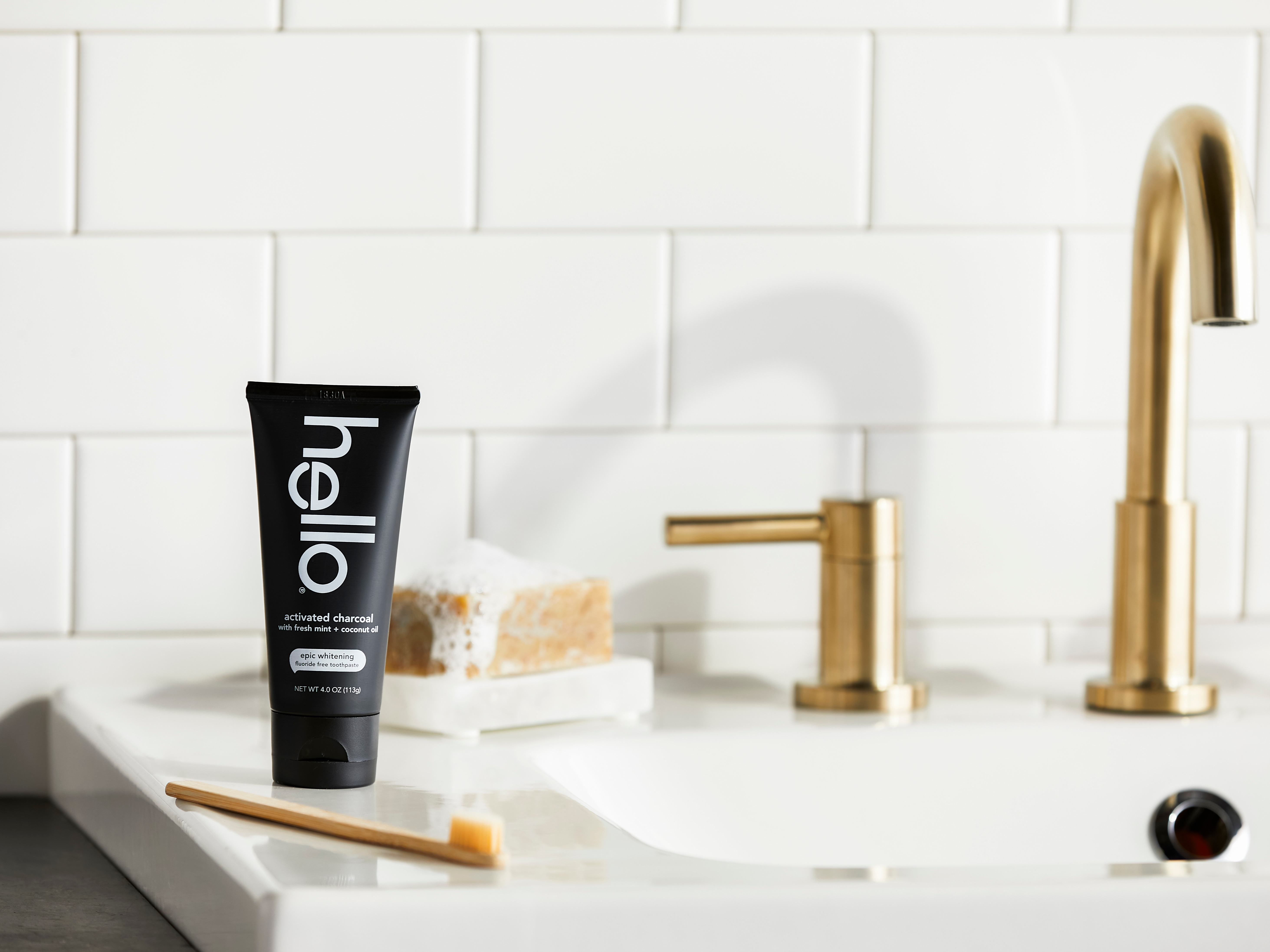 Image of hello Charcoal Toothpaste and bamboo toothbrush on side of sink with gold faucet