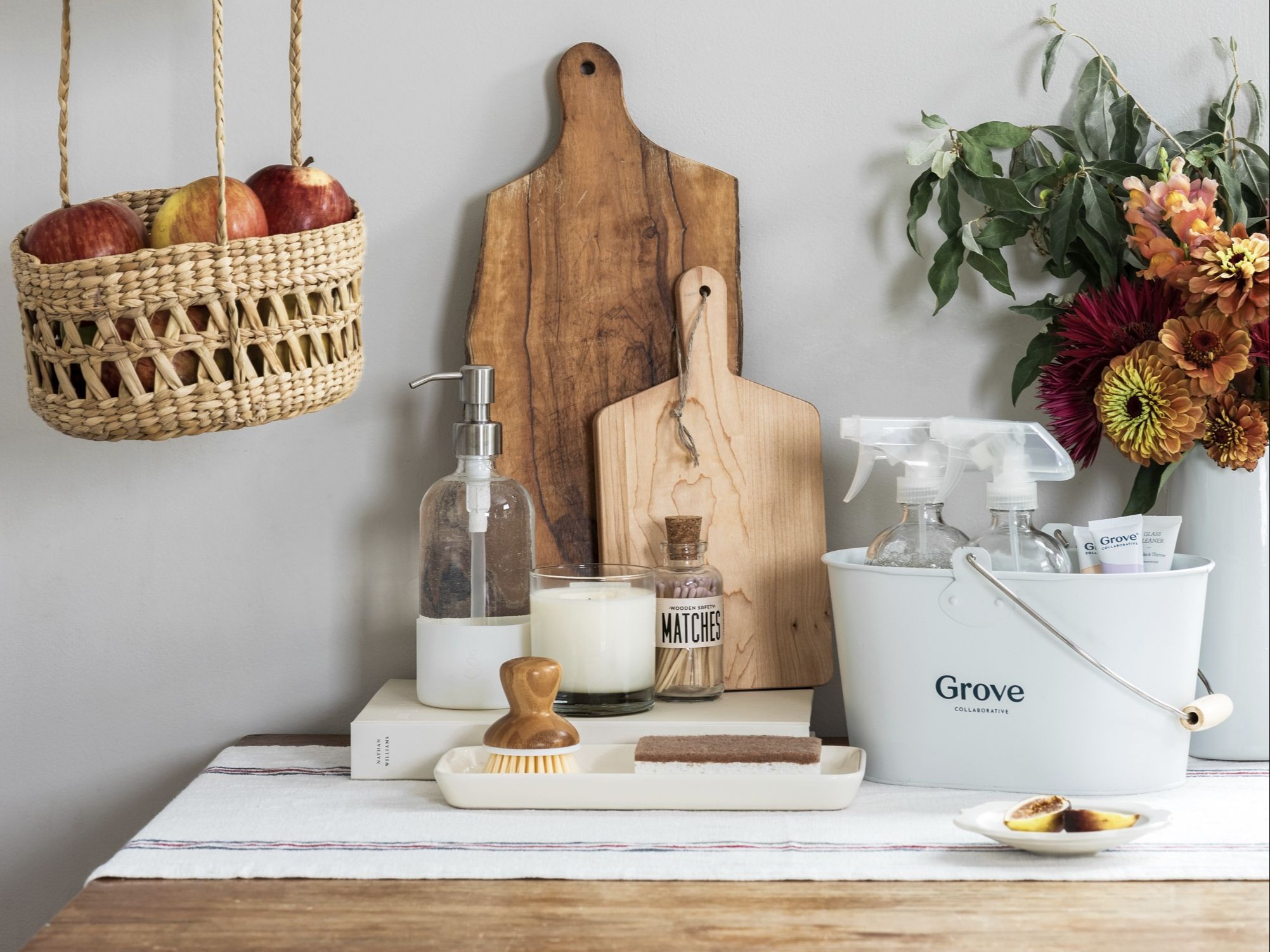 Image of Grove cleaning supplies and products on wooden counter next to cutting board and hanging basket of apples