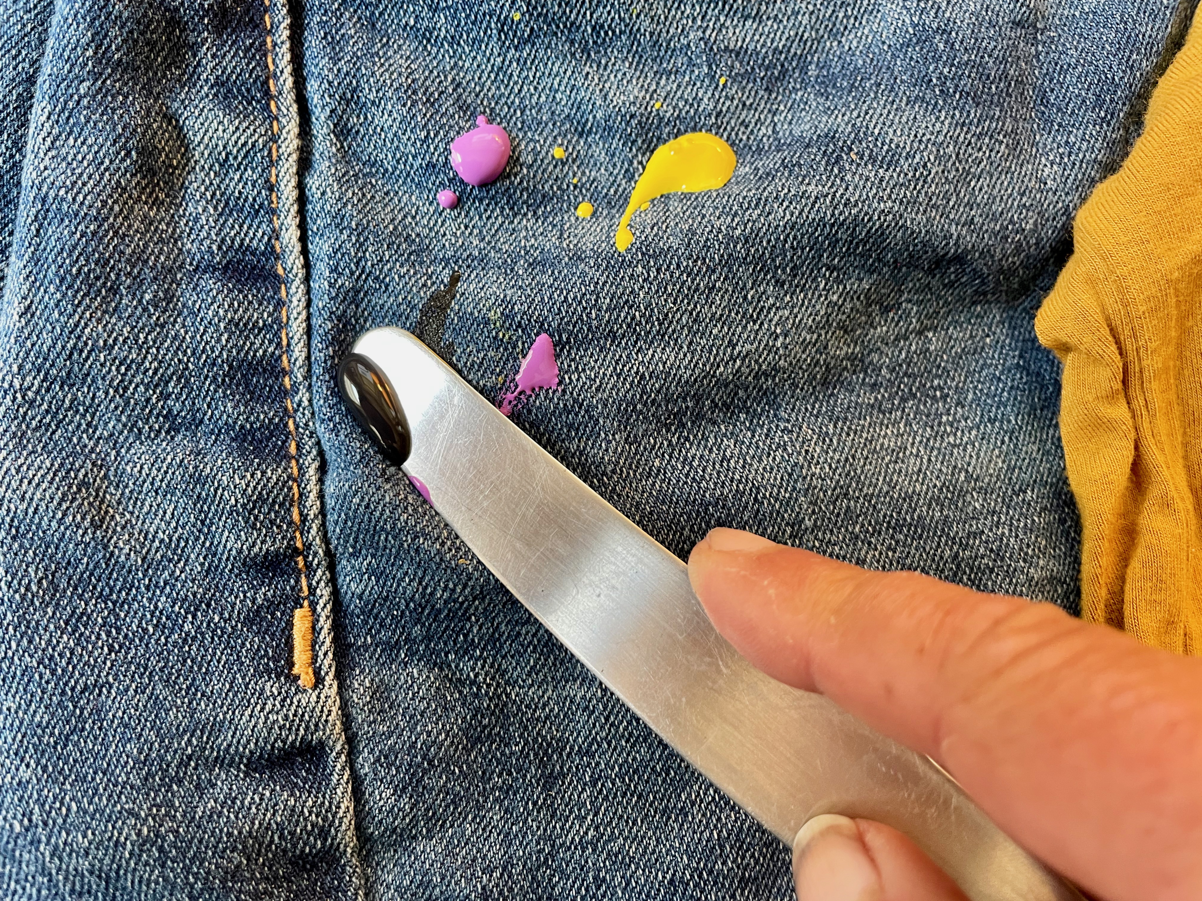 someone scraping fresh paint off of a pair of jeans