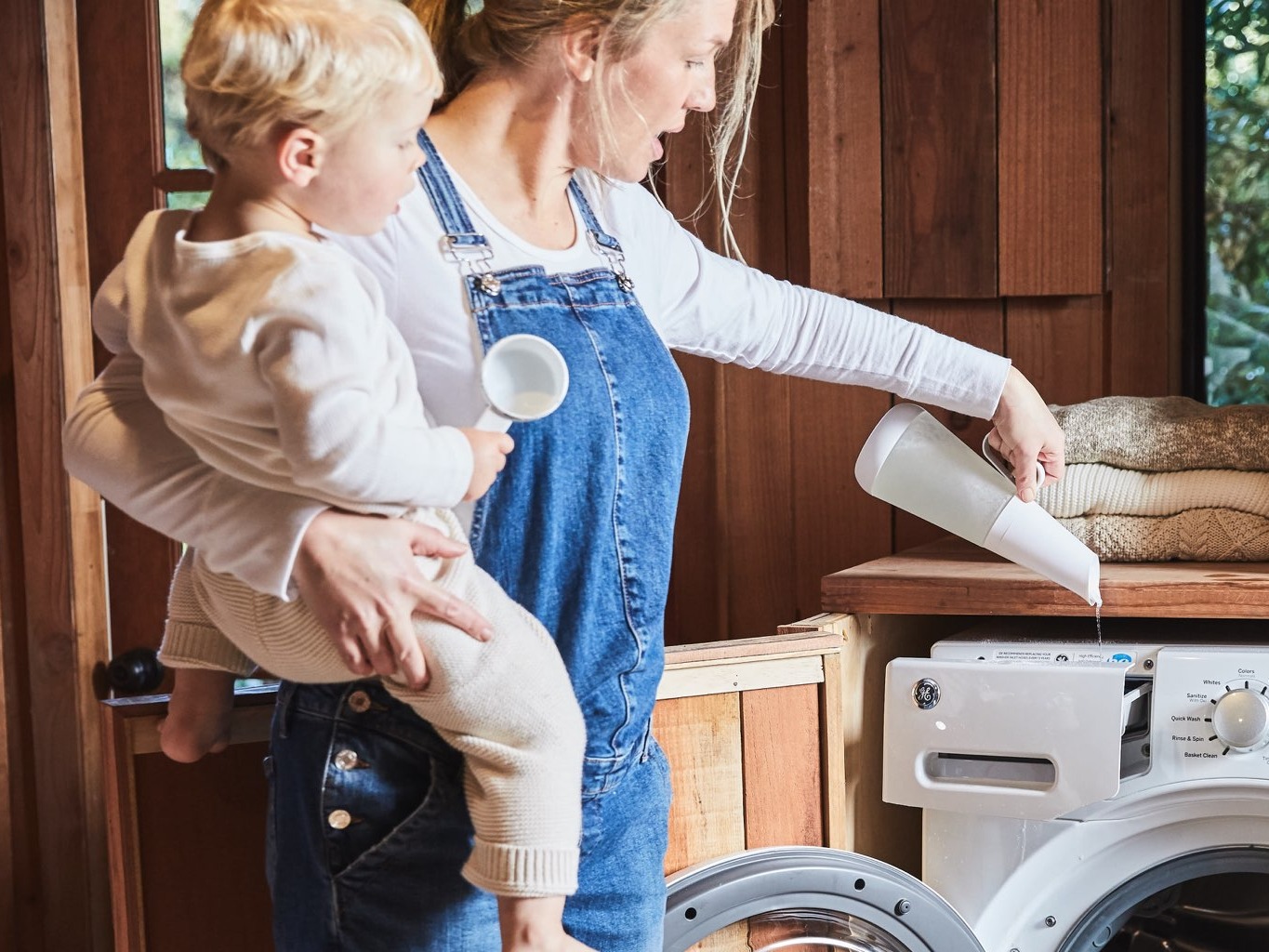 Adult holds a young child while they clean their front loading washing machine