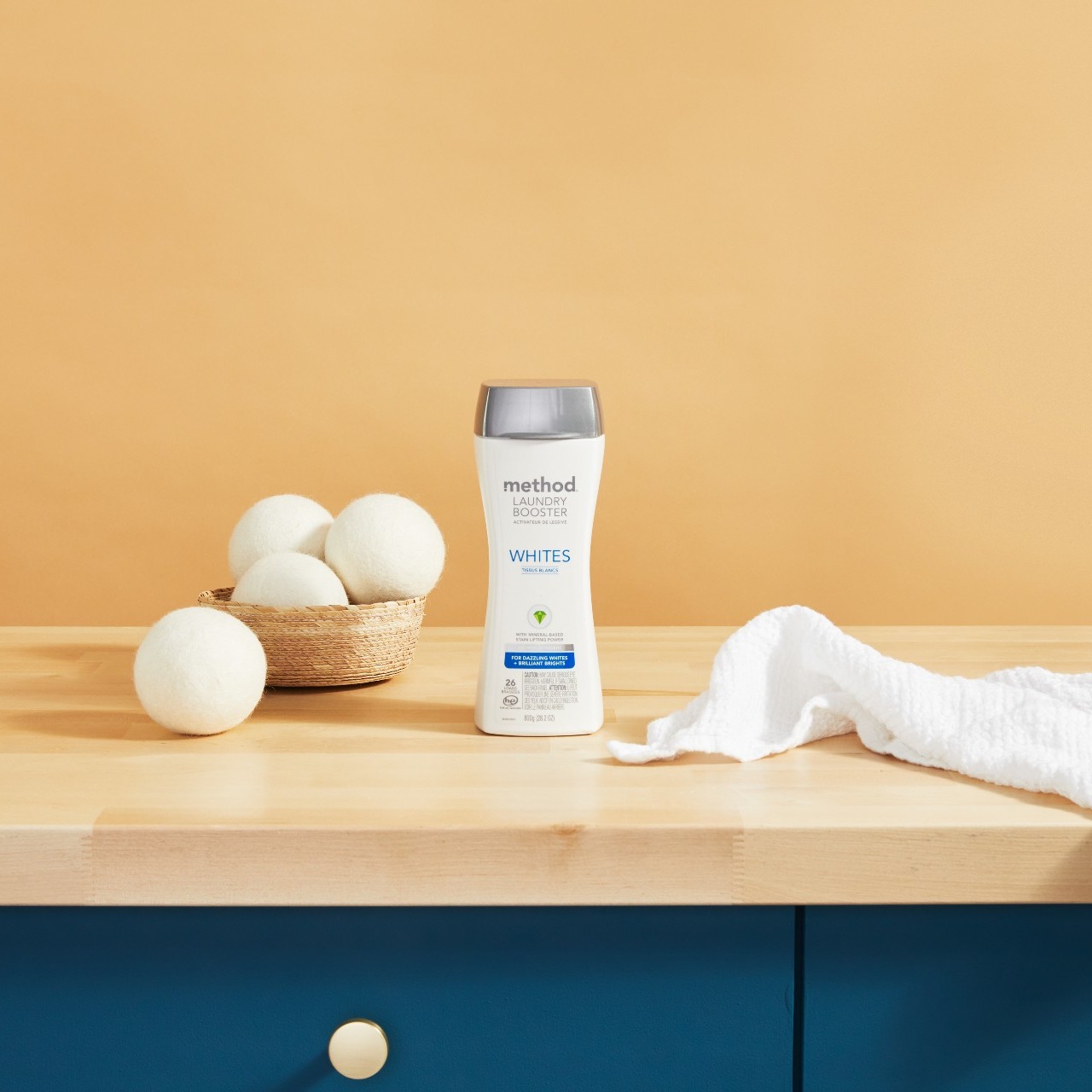 A bottle of method Laundry Booster on a table with wool dryer balls.