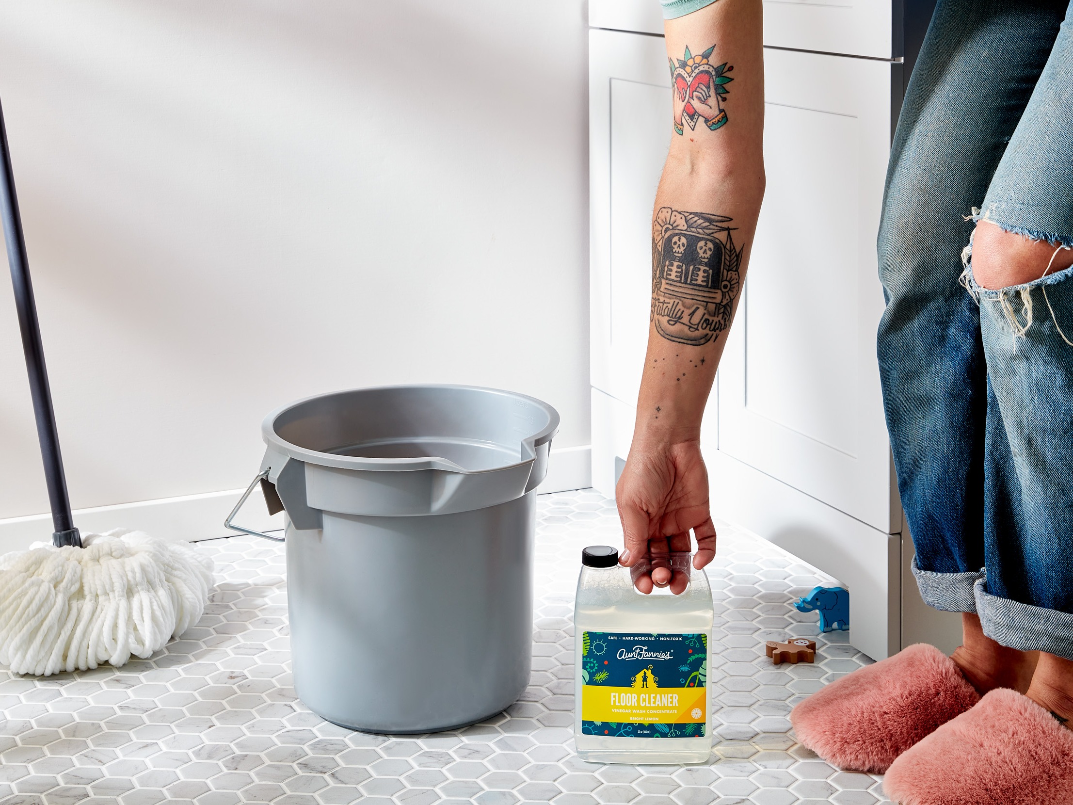Image of person reaching down to get Aunt Fannie's floor cleaner bottle next to bucket and mop