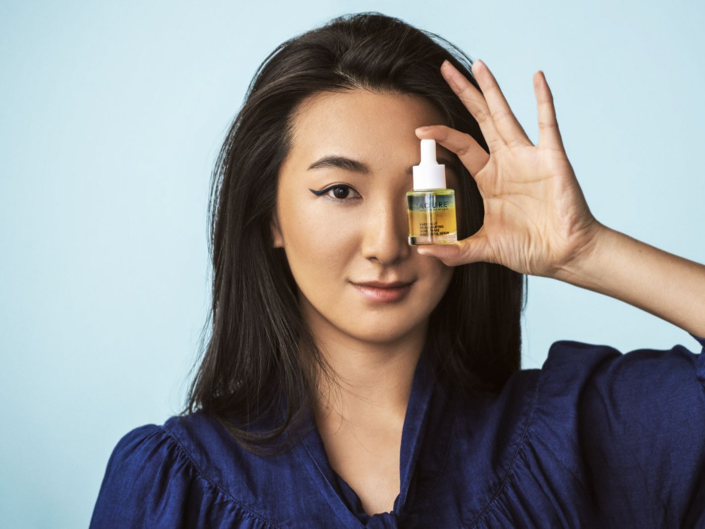 Image of Asian woman holding bottle of oil with dropper up over her left eye