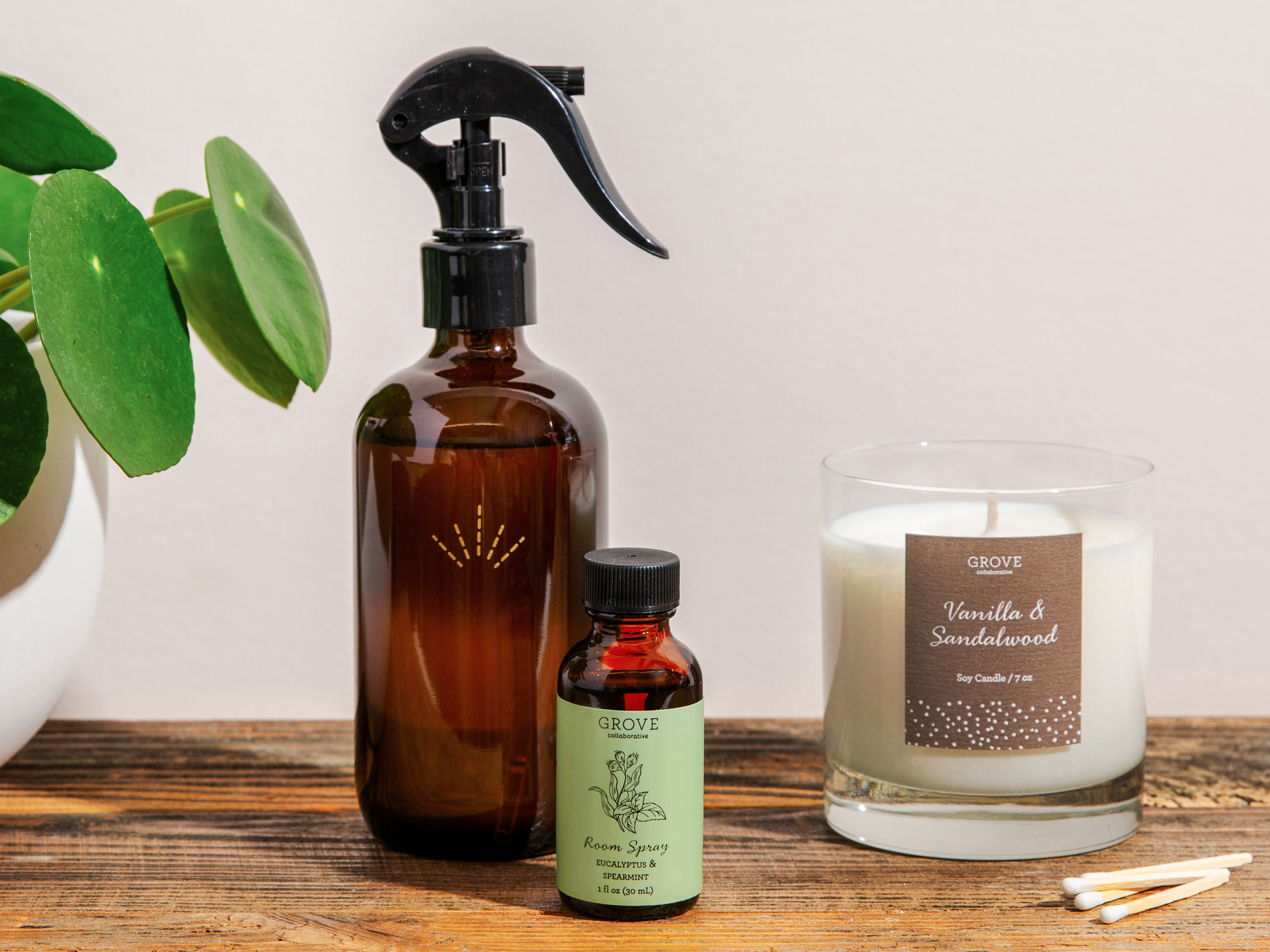 Spray bottle, essential oil dropper and candle on a table with a plant