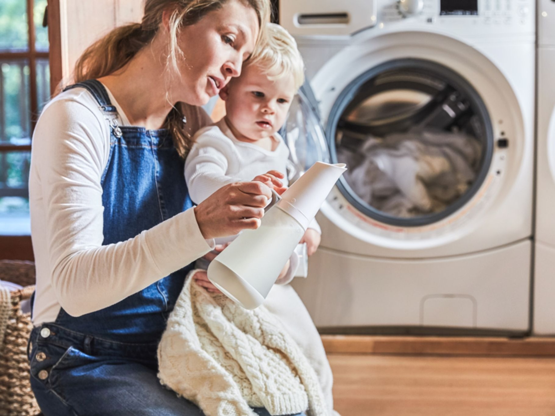 Woman and child holding laundry detergent dispenser in front of washer and dryer