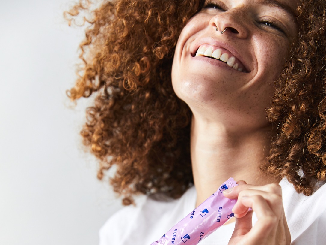 woman throwing her head back smiling while holding a Sustain tampon in pink wrapper
