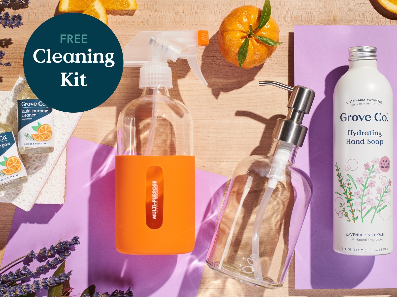 Image of orange glass spray bottle, glass hand soap bottle, refillable aluminum Grove Co. hand soap bottle and cleaning concentrate bottles with Free Cleaning Kit callout